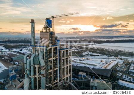 Aerial view of cement plant with high factory structure and tower crane at industrial production area at sunset. Aerial view of cement plant with high factory structure and tower crane at industrial production area at sunset. 85036428