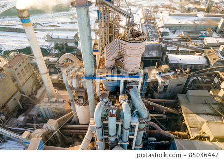 Aerial view of cement plant with high factory structure and tower crane at industrial production area at sunset. Aerial view of cement plant with high factory structure and tower crane at industrial production area at sunset. 85036442