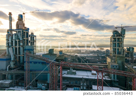 Aerial view of cement plant with high factory structure and tower crane at industrial production area at sunset. Aerial view of cement plant with high factory structure and tower crane at industrial production area at sunset. 85036443