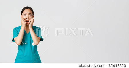 Covid-19, healthcare workers and preventing virus concept. Scared insecure asian female doctor, nurse in scrubs starts to panic from fear, biting fingernails and looking horrified, white background Covid-19, healthcare workers and preventing virus concept. Scared insecure asian female doctor, nurse in scrubs starts to panic from fear, biting fingernails and looking horrified, white background 85037830