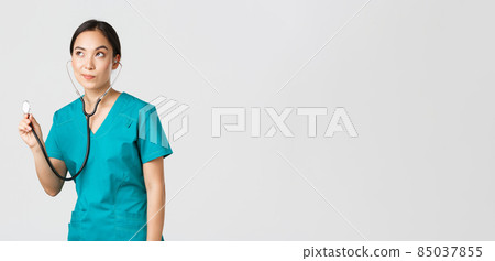 Covid-19, healthcare workers and preventing virus concept. Young focused asian female doctor, physician in scrubs, examine patient lungs, using stethoscope, standing thoughtful white background 85037855