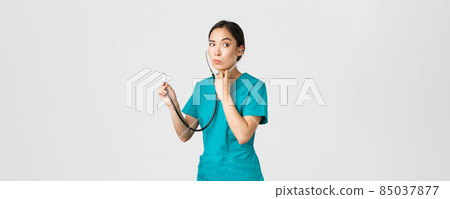 Covid-19, healthcare workers and preventing virus concept. Intrigued asian female doctor, physician in scrubs, looking away thoughtful, listening to patient lungs with stethoscope, white background Covid-19, healthcare workers and preventing virus concept. Intrigued asian female doctor, physician in scrubs, looking away thoughtful, listening to patient lungs with stethoscope, white background 85037877