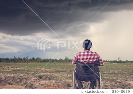 Young disabled man with field background.He is sitting on wheelchair.He is looking into dark sky.despair,lonely,hope.Photo concept depression and Patient. Young disabled man with field background.He is sitting on wheelchair.He is looking into dark sky.despair,lonely,hope.Photo concept depression and Patient. 85040629