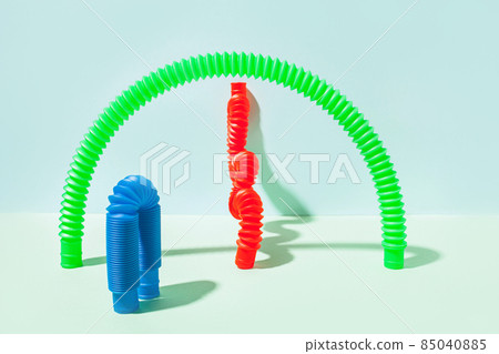 The curved pop tube stands leaning against the wall. Modern still life with antistress toy The curved pop tube stands leaning against the wall. Modern still life with antistress toy 85040885