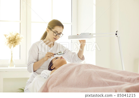 Woman cosmetologist use lens lamp do beauty procedures for female client in aesthetic medicine salon. Beautician doctor make skincare treatment for patient in cosmetic saloon. Cosmetology. 85041215