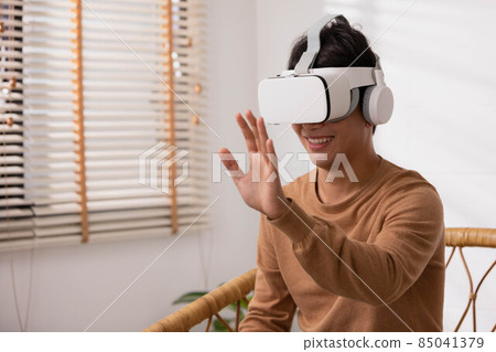 Asian man wearing virtual reality goggles in modern coworking studio. Smartphone using with VR headset. Asian man wearing virtual reality goggles in modern coworking studio. Smartphone using with VR headset. 85041379