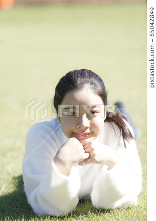 放鬆在草坪的一名年輕微笑的婦女的前面 放鬆在草坪的一名年輕微笑的婦女的前面 85042849
