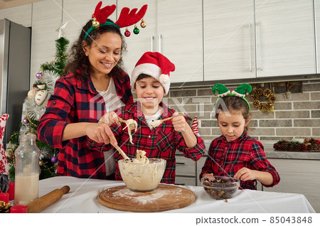 Charming woman, mother teaches children how to make dough for Christmas baking. Adorable European children cook with their mother in kitchen. Concept to share a happy time during Christmas holidays Charming woman, mother teaches children how to make dough for Christmas baking. Adorable European children cook with their mother in kitchen. Concept to share a happy time during Christmas holidays 85043848