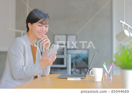 Business woman looking at her smartphone with her hand on her chin 1 Business woman looking at her smartphone with her hand on her chin 1 85044689