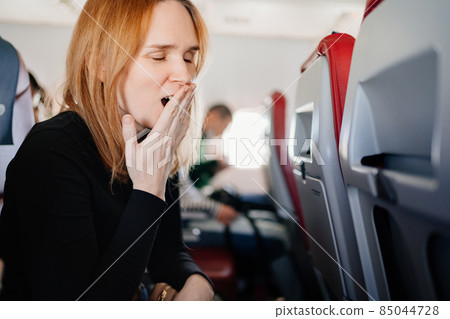 a sleepy woman yawns in an airplane seat. long flights. a sleepy woman yawns in an airplane seat. long flights. 85044728