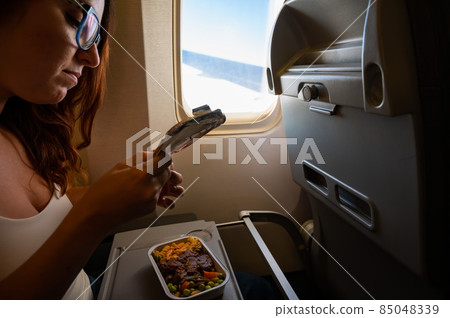 Caucasian woman flying in economy class and eating lunch from a tray table on board the plane. 85048339