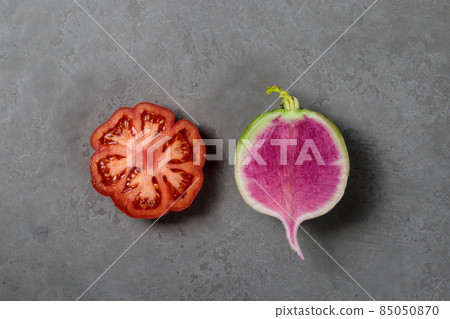 Ribbed tomato and Chinese radish, cut in half. Close-up on a gray background. Top view 85050870