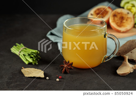 Meat broth with spices and vegetables in a mug, on a wooden board. Close-up. On a black background, horizontal Meat broth with spices and vegetables in a mug, on a wooden board. Close-up. On a black background, horizontal 85050924