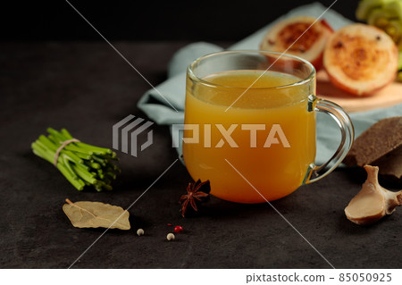 Meat broth with spices and vegetables in a mug. Close-up. On a black background, horizontal with space 85050925