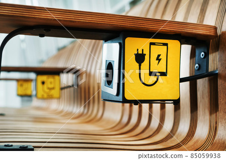 A designer wooden bench with sockets and a yellow sign for charging smartphones in the waiting room. 85059938