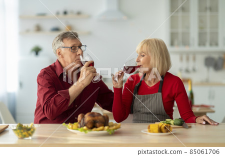 Affectionate senior couple drinking red wine while preparing festive Christmas dinner, making roasted turkey at kitchen Affectionate senior couple drinking red wine while preparing festive Christmas dinner, making roasted turkey at kitchen 85061706