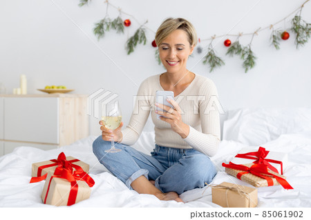 Happy lady using cellphone on Xmas drinking wine 85061902
