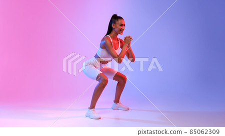 Sporty Lady Doing Deep Squats During Workout On Neon Background Sporty Lady Doing Deep Squats During Workout On Neon Background 85062309