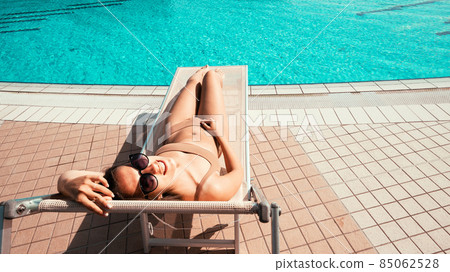 Summer fun beach. Happy young sexy girl in bikini swimsuit, sunglasses on resort chair. Relax lounge at luxury hotel blue water pool. Spa and sunbathing outdoor. Summer fun beach. Happy young sexy girl in bikini swimsuit, sunglasses on resort chair. Relax lounge at luxury hotel blue water pool. Spa and sunbathing outdoor. 85062528