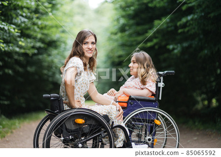 Young women in wheelchairs sitting at summer park Young women in wheelchairs sitting at summer park 85065592