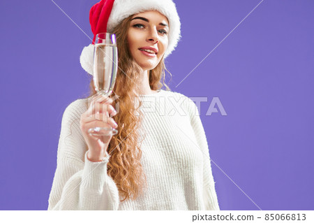 Portrait of happy girl wears in santa hat with glass of champagne on violet background 85066813