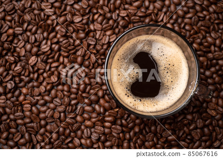 The top view of a coffee cup and group of black coffee beans is the background. Strong black espresso, Grounds of coffee background, texture The top view of a coffee cup and group of black coffee beans is the background. Strong black espresso, Grounds of coffee background, texture 85067616