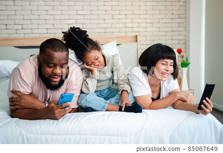 African American girls are not satisfied and sad, sitting in the middle between father and mother. Parents Are using the smartphone and abandoned children. Children need their parents attention. 85067649
