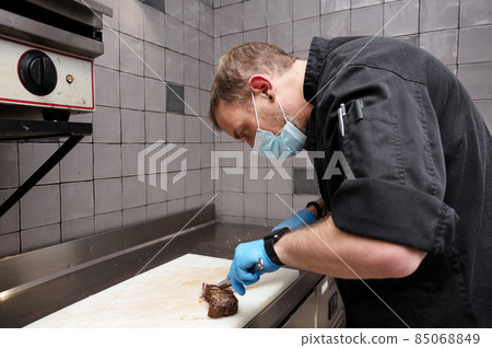Chef cutting juicy steak on a board at commercial kitchen. 85068849