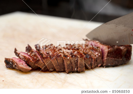Chef cutting juicy steak on a board at commercial kitchen. 85068850