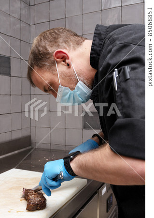 Chef cutting juicy steak on a board at commercial kitchen. 85068851