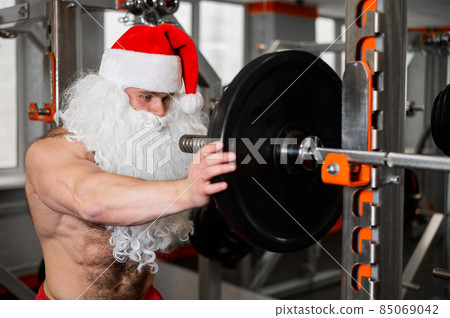 Man in santa claus hat and red shorts posing at the gym. Man in santa claus hat and red shorts posing at the gym. 85069042