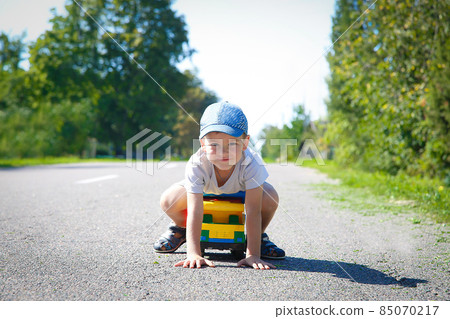 A boy in a baseball cap playing on an asphalt road with a large truck 85070217