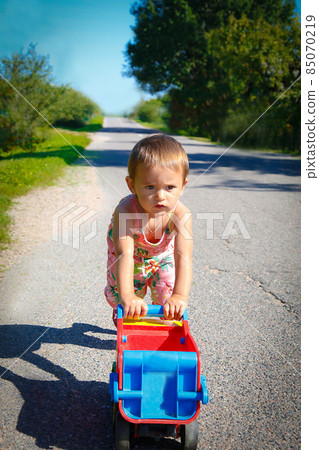 Little girl alone on the road playing with a big truck 85070219