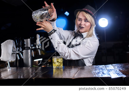 Charming girl bartending adds ingredients to a cocktail in the night club 85070249
