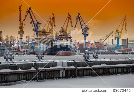 The construction of nuclear icebreakers at magic sunset, cranes of of the Baltic shipyard in a frosty winter day, steam over the Neva river, smooth surface of the river, sky of orange color 85070445