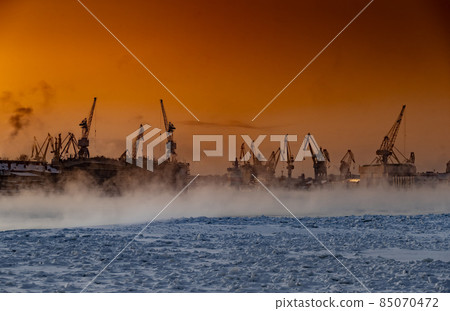 The construction of nuclear icebreakers at magic sunset, cranes of of the Baltic shipyard in a frosty winter day, steam over the Neva river, smooth surface of the river, sky of orange color The construction of nuclear icebreakers at magic sunset, cranes of of the Baltic shipyard in a frosty winter day, steam over the Neva river, smooth surface of the river, sky of orange color 85070472