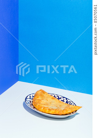 Homemade chebureks with stuffing and herbs in traditional Caucasian plate on blue Homemade chebureks with stuffing and herbs in traditional Caucasian plate on blue 85070561