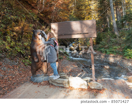 Girl on a background of autumn forest stroking a wooden statue of a bear 85071427