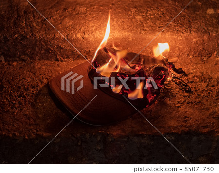 The textile cap burns with a bright fire lying on the concrete steps in the dark. Image in brown shades 85071730