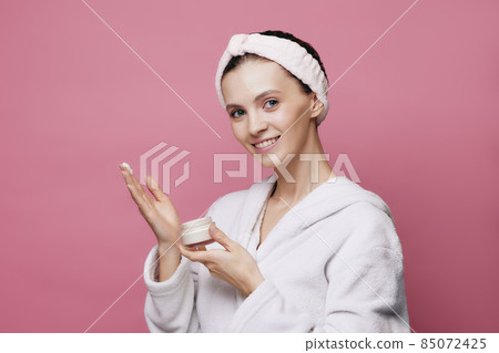 Young girl in bathrobe holding face cream 85072425