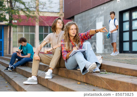 Teenage boy and girl sitting on steps near school Teenage boy and girl sitting on steps near school 85073825