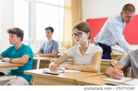 Teenage schoolgirl in glasses writing in workbook during lesson Teenage schoolgirl in glasses writing in workbook during lesson 85074160