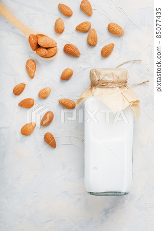 Milk from organic almonds in a transparent bottle with a scattering of seeds and a wooden spoon on a light background 85077435