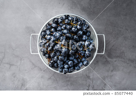 Sweet black grapes in a metal bowl on a dark textured background. 85077440