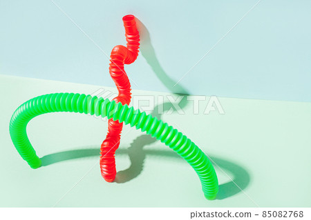 The curved pop tube stands leaning against the wall. Modern still life with antistress toy The curved pop tube stands leaning against the wall. Modern still life with antistress toy 85082768
