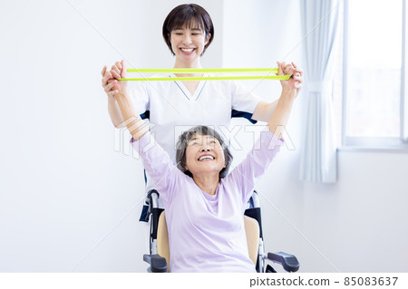 Nursing image: Senior woman exercising with a rubber tube and a physiotherapist Photographing cooperation: Japanese Language School attached to Chuo Institute of Technology Nursing image: Senior woman exercising with a rubber tube and a physiotherapist Photographing cooperation: Japanese Language School attached to Chuo Institute of Technology 85083637