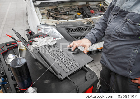 Mechanic using computer for diagnostics engine. Repairing car. Blur garage auto repair service in background. Mechanic using computer for diagnostics engine. Repairing car. Blur garage auto repair service in background. 85084407