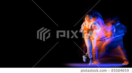 Sportive young girl in white costume dancing hip-hop dance isolated on dark background at dance hall in neon mixed light. 85084659