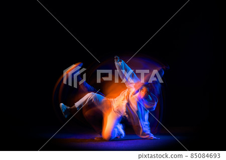 Portrait of young dark skinned flexible girl in white hoodie dancing hip-hop isolated on dark background in purple neon mixed light. Portrait of young dark skinned flexible girl in white hoodie dancing hip-hop isolated on dark background in purple neon mixed light. 85084693