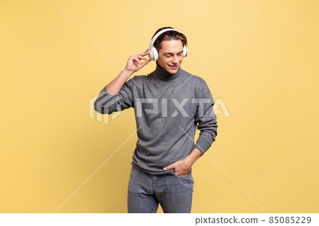 One young handsome man, student listening to music in headphones isolated on yellow studio background. 85085229